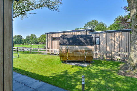 Vue extérieure d’un lodge de luxe avec façade en bois moderne et sauna tonneau à Drentse Weelde, Pays-Bas.