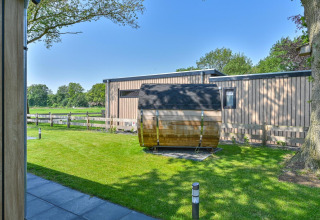 Vista exterior de un lodge de lujo con fachada de madera moderna y sauna en barril en Drentse Weelde, Países Bajos.