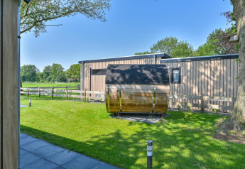 Vue extérieure d’un lodge de luxe avec façade en bois moderne et sauna tonneau à Drentse Weelde, Pays-Bas.