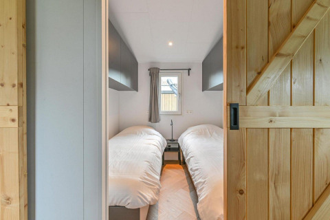 Moderne slaapkamer met twee eenpersoonsbedden, houten schuifdeur en venster bij Drentse Weelde lodge.