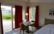 Innenraum der Comfort Lodge Tiny House bei Kompas Camping Nieuwpoort mit Esstisch und roten Vorhängen.