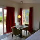 Interior of Comfort Lodge tiny house at Kompas Camping Nieuwpoort, Belgium, with table and red curtains.