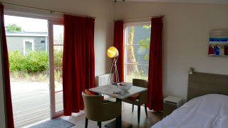 Innenraum der Comfort Lodge Tiny House bei Kompas Camping Nieuwpoort mit Esstisch und roten Vorhängen.