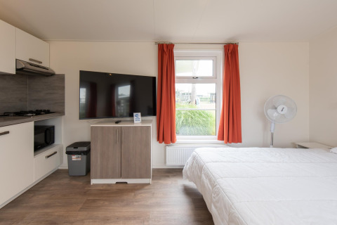Moderna tiny house Comfort Lodge en Kompas Camping Nieuwpoort, Bélgica, con TV, cama y pequeña cocina.