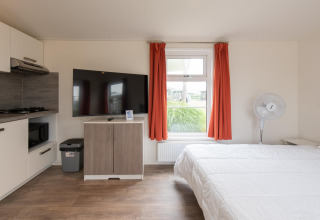 Moderna tiny house Comfort Lodge en Kompas Camping Nieuwpoort, Bélgica, con TV, cama y pequeña cocina.
