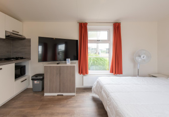Moderna tiny house Comfort Lodge en Kompas Camping Nieuwpoort, Bélgica, con TV, cama y pequeña cocina.