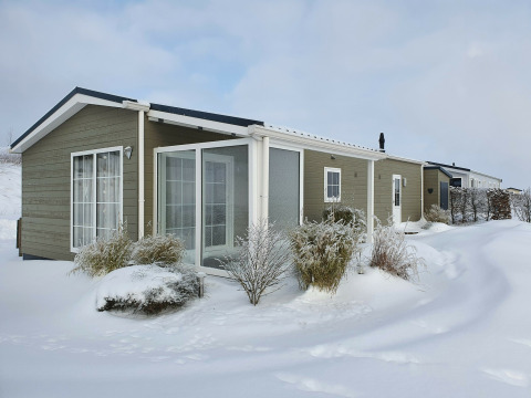 Chalet Marron im Camping & Ferienpark Brilon, Deutschland, im Winter mit verschneiter Landschaft und Büschen.