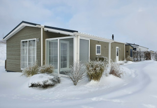 Chalet Marron im Camping & Ferienpark Brilon, Deutschland, im Winter mit verschneiter Landschaft und Büschen.