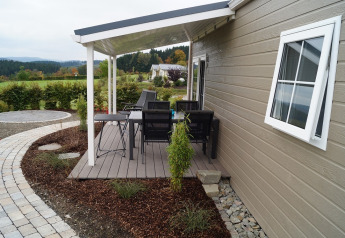 Terraza cubierta en el Chalet Marron del Camping & Ferienpark Brilon, Alemania, con mesa, sillas y paisaje rural.