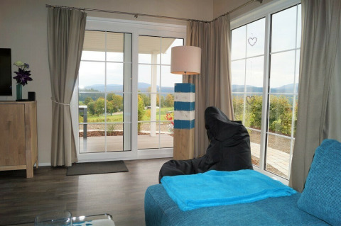 Woonkamerzicht in Chalet Marron, Camping & Ferienpark Brilon, Duitsland, uitkijkend op heuvelachtig landschap.
