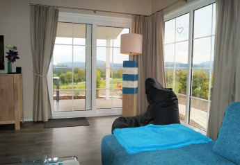 Stue med store vinduer i Chalet Marron, Camping & Ferienpark Brilon, med udsigt over det tyske landskab.