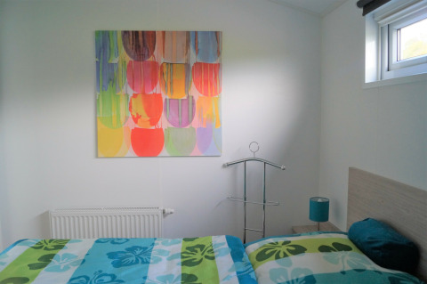 Helles Schlafzimmer im Chalet Marron mit buntem Gemälde, moderner Bettwäsche und Fenster in Deutschland.