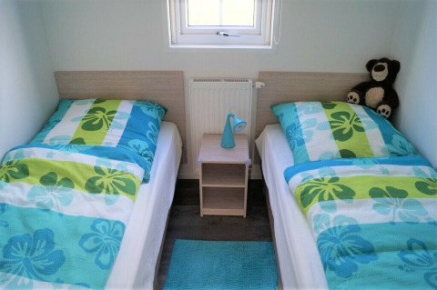 Zwei Einzelbetten mit bunten Decken, Nachttisch, blauer Lampe und Teddy im Chalet Marron, Brilon.