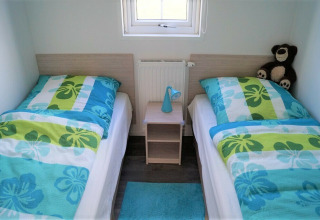 Zwei Einzelbetten mit bunten Decken, Nachttisch, blauer Lampe und Teddy im Chalet Marron, Brilon.