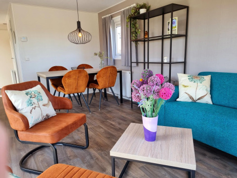 Knusse woonkamer in Chalet Brilon met oranje stoelen, bloemen en tafel op Camping Brilon, Duitsland.