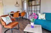 Knusse woonkamer in Chalet Brilon met oranje stoelen, bloemen en tafel op Camping Brilon, Duitsland.