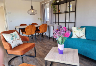 Acogedora sala en Chalet Brilon con sillas naranjas, flores y comedor en Camping Brilon, Alemania.