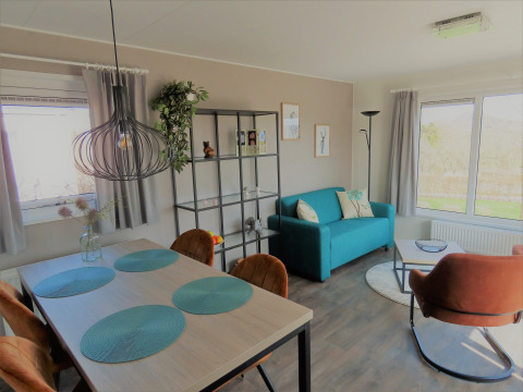 Salón moderno en Chalet Brilon con sofá turquesa, mesa de comedor y grandes ventanas en Camping Brilon.