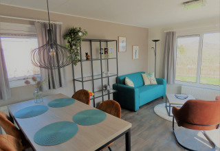 Salón moderno en Chalet Brilon con sofá turquesa, mesa de comedor y grandes ventanas en Camping Brilon.