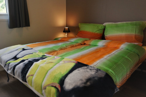 Cama doble con ropa de cama colorida y lámpara de noche en una habitación de Chalet Brilon, Alemania.