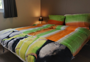 Double bed with colorful bedding and a night lamp in a cozy room at Chalet Brilon, Germany.