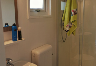 Baño moderno con ducha, lavabo, inodoro y toalla verde colgada en Chalet Brilon, Alemania.