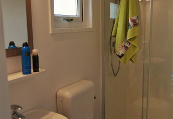 Modern bathroom with shower, sink, toilet, and green towel hanging in Chalet Brilon at a German campsite.