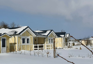 Casas móviles amarillas cubiertas de nieve en Chalet Limonet, Camping & Ferienpark Brilon, Alemania, en invierno.