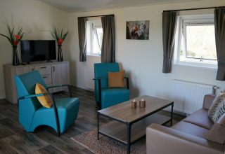 Sala moderna en Chalet Limonet en Camping & Ferienpark Brilon, con sillones azules y TV en Alemania.