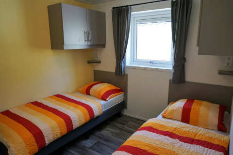 Habitación en Chalet Limonet con dos camas individuales, ropa de cama colorida y ventana, Camping & Ferienpark Brilon.