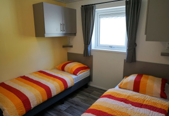 Habitación en Chalet Limonet con dos camas individuales, ropa de cama colorida y ventana, Camping & Ferienpark Brilon.