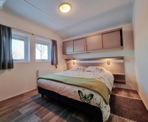 Dormitorio en Chalet Limonet con cama doble, ventanas y almacenamiento en Camping & Ferienpark Brilon, Alemania.