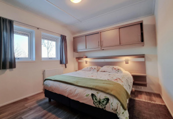 Dormitorio en Chalet Limonet con cama doble, ventanas y almacenamiento en Camping & Ferienpark Brilon, Alemania.