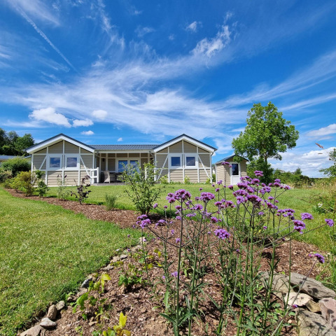 Vista del mobil home Chalet Limonet y jardín en Camping & Ferienpark Brilon bajo cielo azul brillante en Alemania.