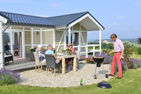 Cuatro adultos disfrutan de una barbacoa en la cabaña Calcelux, Camping & Ferienpark Brilon, Alemania.