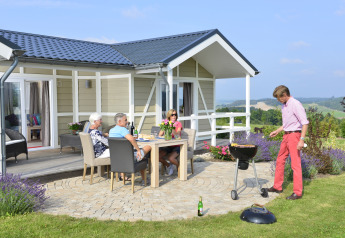 Quatre adultes profitent d’un barbecue devant la cabane Calcelux au Camping & Ferienpark Brilon en Allemagne.