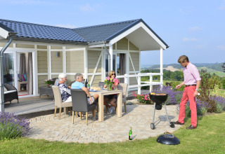 Cuatro adultos disfrutan de una barbacoa en la cabaña Calcelux, Camping & Ferienpark Brilon, Alemania.