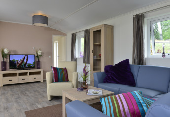 Sala luminosa en la cabaña Calcelux de Camping & Ferienpark Brilon, Alemania, con sofá, sillón y televisor.