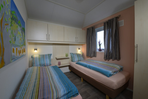 Dos camas individuales con ropa de cama a rayas en una acogedora habitación de Calcelux, Camping Brilon.