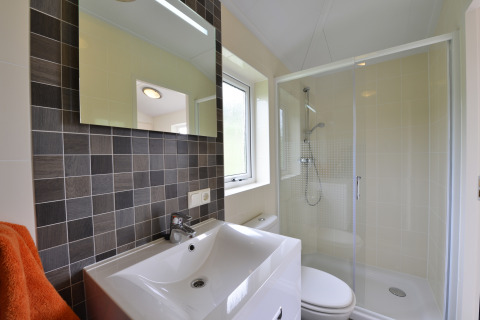 Baño moderno con ducha, mampara de cristal, lavabo, espejo y ventana en la cabaña Calcelux, Alemania.