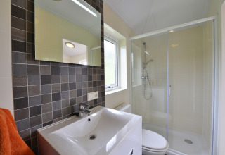 Baño moderno con ducha, mampara de cristal, lavabo, espejo y ventana en la cabaña Calcelux, Alemania.