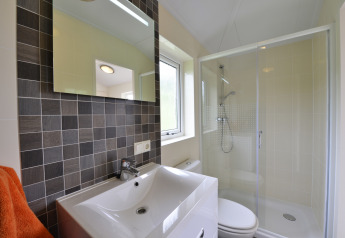 Baño moderno con ducha, mampara de cristal, lavabo, espejo y ventana en la cabaña Calcelux, Alemania.