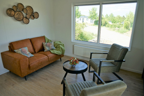 Wohnzimmer im Chalet Alme im Camping & Ferienpark Brilon mit Sofa, Sesseln und großem Fensterblick.
