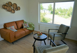 Wohnzimmer im Chalet Alme im Camping & Ferienpark Brilon mit Sofa, Sesseln und großem Fensterblick.