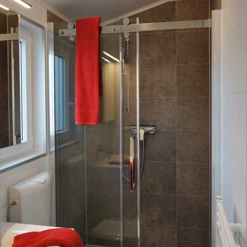 Moderne douchecabine met glazen deur en rode handdoek in Chalet Alme, Camping & Ferienpark Brilon, Duitsland.