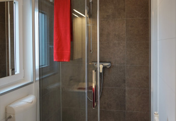 Cabina de ducha moderna con puerta de vidrio y toalla roja en Chalet Alme, Camping & Ferienpark Brilon, Alemania.