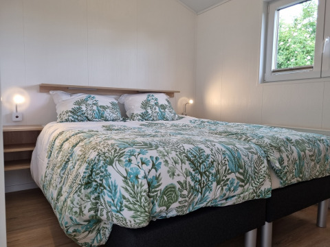 Schlafzimmer im Chalet Alme mit Doppelbett, botanischer Bettwäsche und Fenster im Ferienpark Brilon.