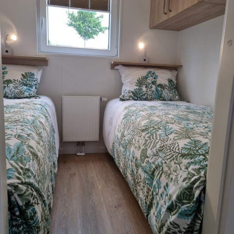 Zwei Einzelbetten mit grüner Blattbettwäsche, Holzfußboden und Fenster in einem kompakten Zimmer.