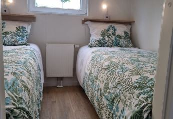 Dos camas individuales con colchas de hojas verdes en una pequeña habitación con suelo de madera y ventana.