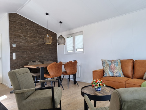 Moderne woonkamer in Chalet Alme met bruin salon, eethoek, groene stoelen en sierkussens.